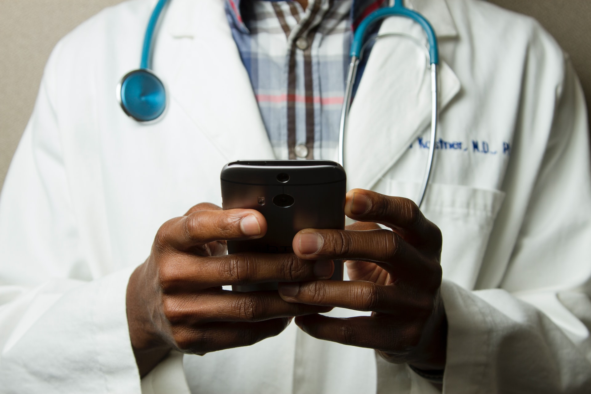 Doctor in white coat with stethoscope using mobile phone